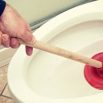 man-fixing-clogged-toilet-with-plunger